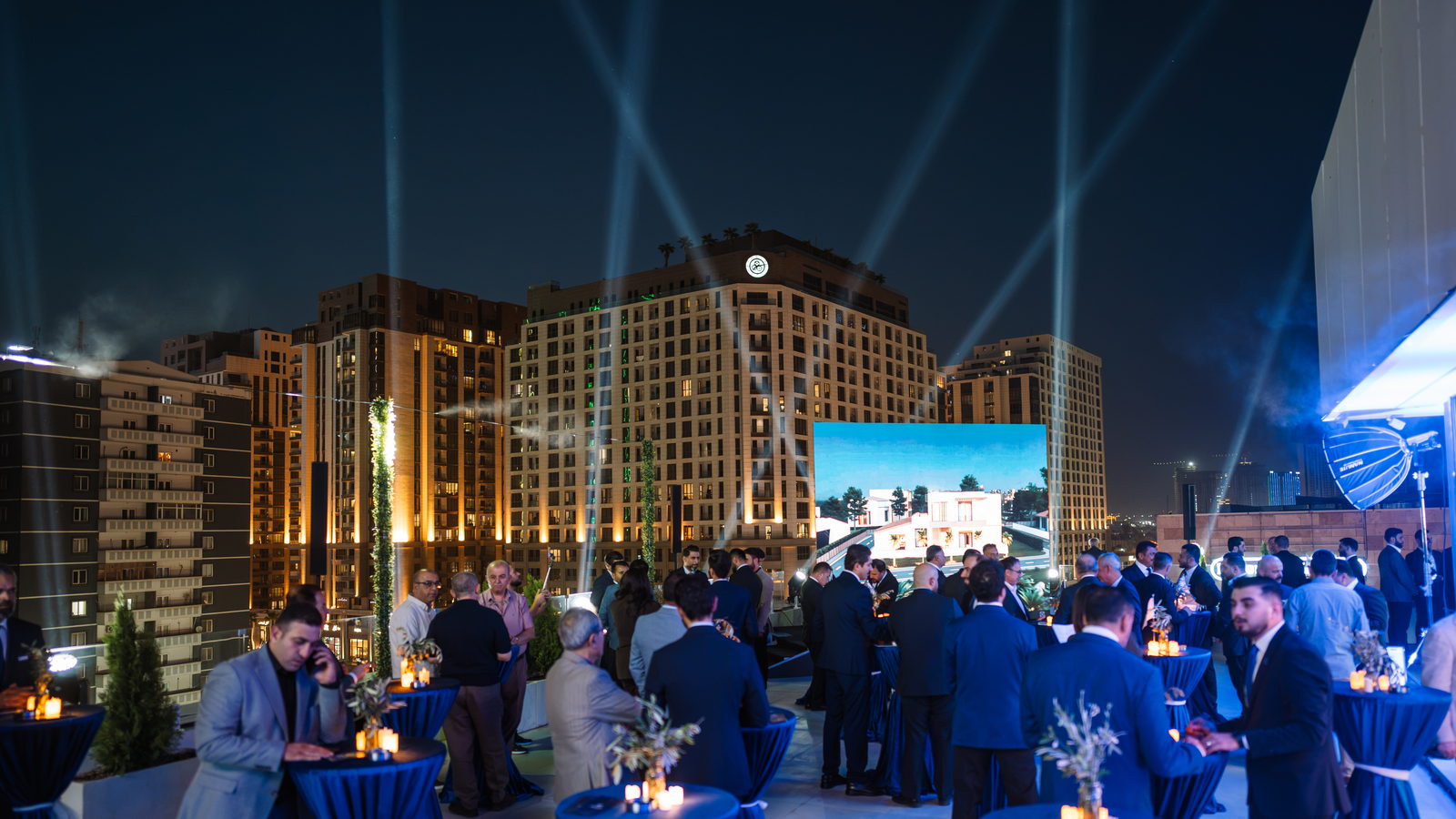 The terrace at dusk, searchlights over the gold-lit towers and the wall already alight